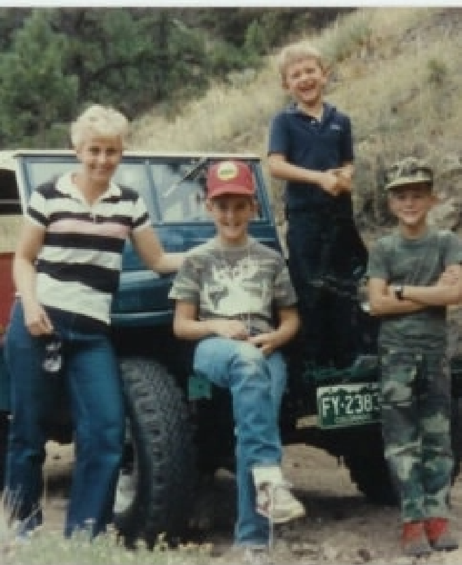 Group of four people posing outdoors beside a jeep; an adult woman and three children, one sitting on the jeep's hood, capturing a perfect moment for the Barney Brothers.