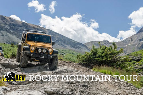 A yellow off-road vehicle from AEV navigates rocky terrain with mountains in the background. Text: AEV Rocky Mountain Tour.