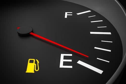Close-up of a car’s fuel gauge with the needle on empty and a yellow low fuel warning light illuminated.