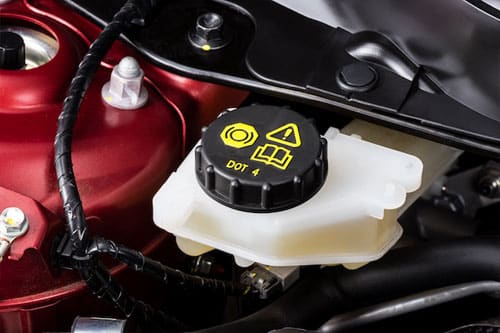 Close-up of a car's brake fluid reservoir with a DOT 4 label on the cap, nestled among engine components.