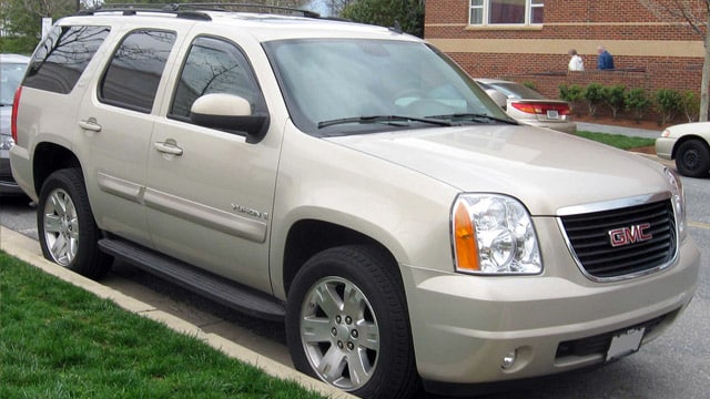 A beige GMC Yukon SUV is parked by the curb on a quiet residential street.