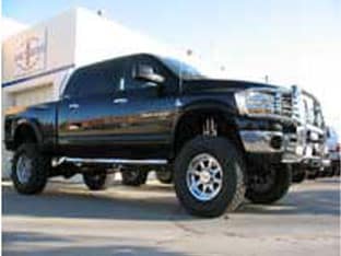 A black lifted pickup truck with chrome details, clearly one of the top customer rigs, parked outside a building, showcasing its large wheels and elevated stance.