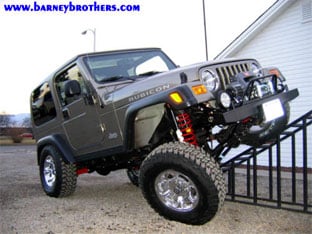 A modified Jeep Wrangler Rubicon on off-road tires climbing a metal grate ramp showcases the impressive capabilities of our customer rigs. Visit us at barneybrothers.com.