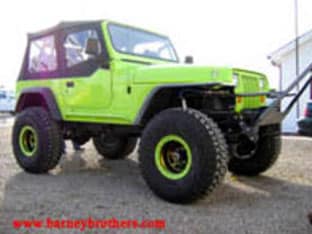 Lime green off-road vehicle with large tires and black soft top roof parked on gravel, showcasing one of our proud customer rigs.