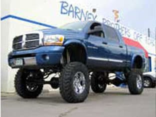 Lifted blue pickup truck with large tires, part of our finest customer rigs, parked outside a building with a "Barney" sign visible in the background.