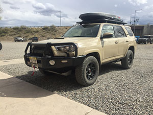 Beige Toyota SUV with roof rack and front bull bar parked on gravel under a cloudy sky.