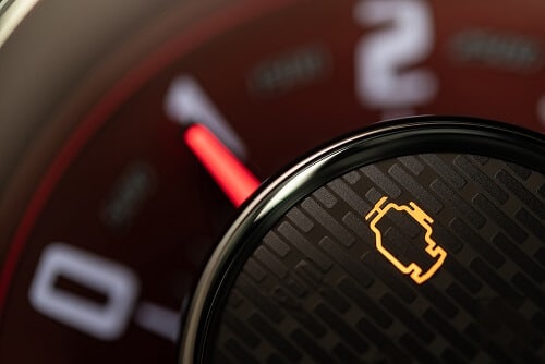 Close-up of a car dashboard showing a lit check engine light on a dark, textured background, hinting at the need for diagnostics.