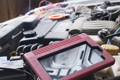 A diagnostics tablet lies on the engine of a car, surrounded by various wires and engine components.