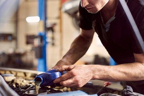 A mechanic meticulously performs an oil change, pouring fresh oil into a car engine in a well-organized garage.