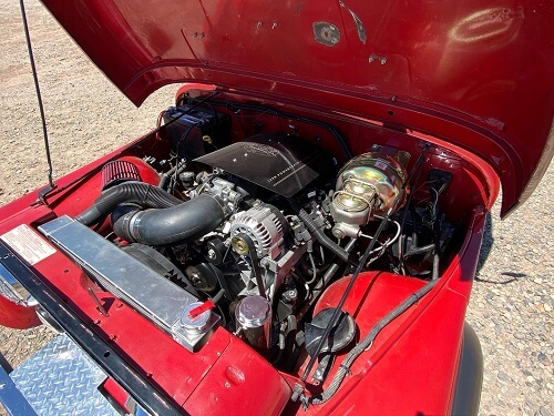 Engine bay of a red classic car with the hood open, showcasing various engine components and parts, highlighting the meticulous engine repair work that keeps this vintage beauty running smoothly.