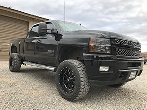 A black Chevrolet truck is parked on a gravel surface in front of a beige building under a cloudy sky.