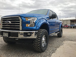 A lifted blue Ford F-150 truck parked on a gravel lot under a cloudy sky, showcasing the power and presence of this iconic vehicle.