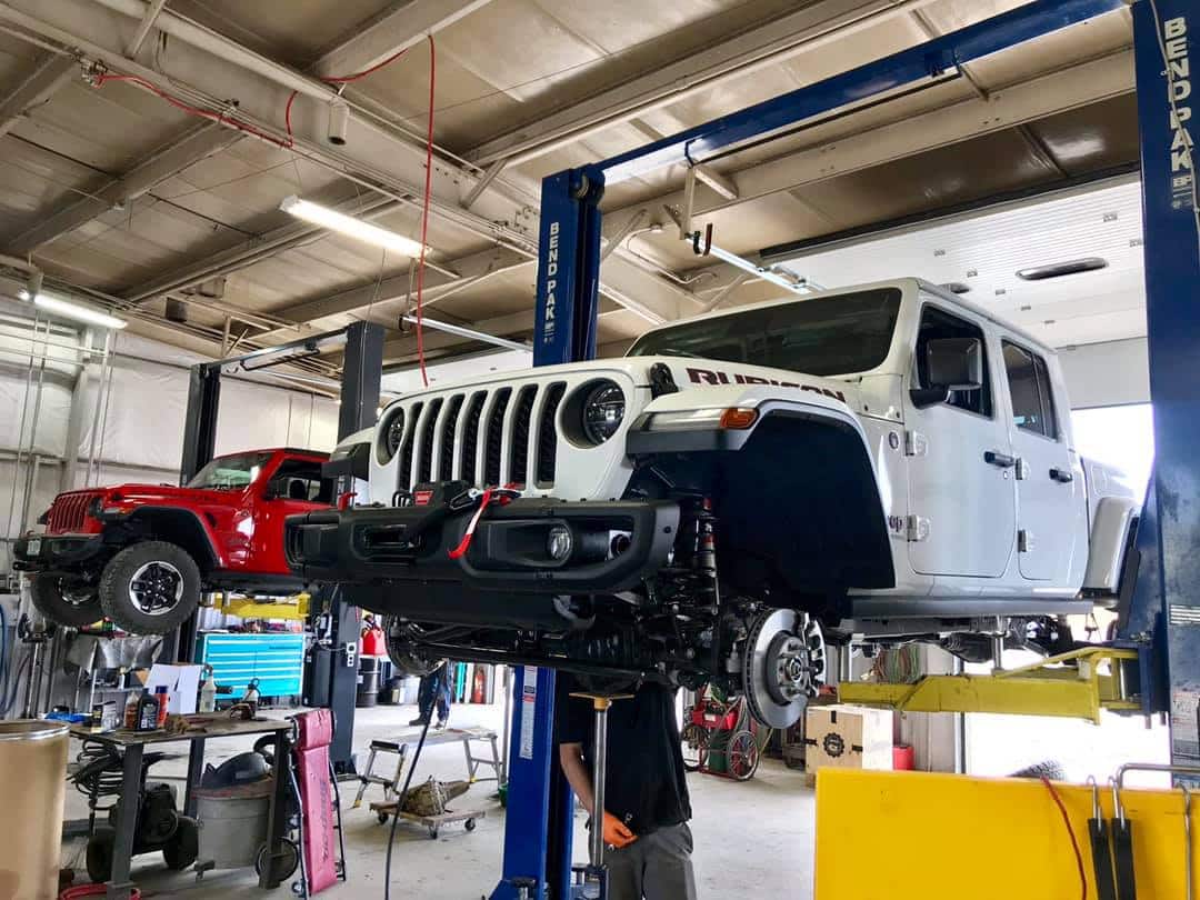 White Jeep Rubicon and red Jeep Wrangler are elevated on car lifts in an auto repair shop, undergoing preventative maintenance to ensure peak performance and longevity.