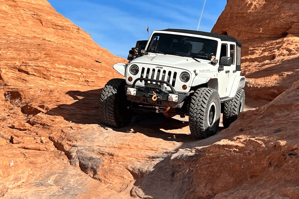 4x4 alignment service, wheel alignment, Grand Junction, CO, Barney Brothers Off-Road and Repair. White Jeep Rubicon navigating a rugged desert terrain, highlighting off-road repair and alignment needs.